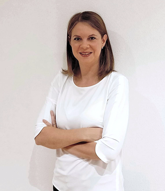 Marina Weiß1 mit glattem braunem Haar, selbstbewusst lächelnd in einem weißen Hemd