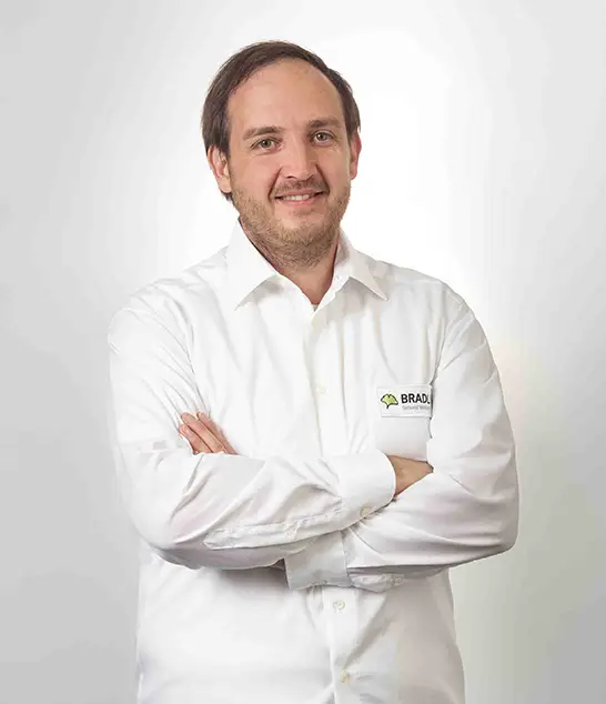 Bauleiter Sebastian Schnurrer in weißem Hemd, lächelnd mit verschränkten Armen vor hellem Hintergrund.