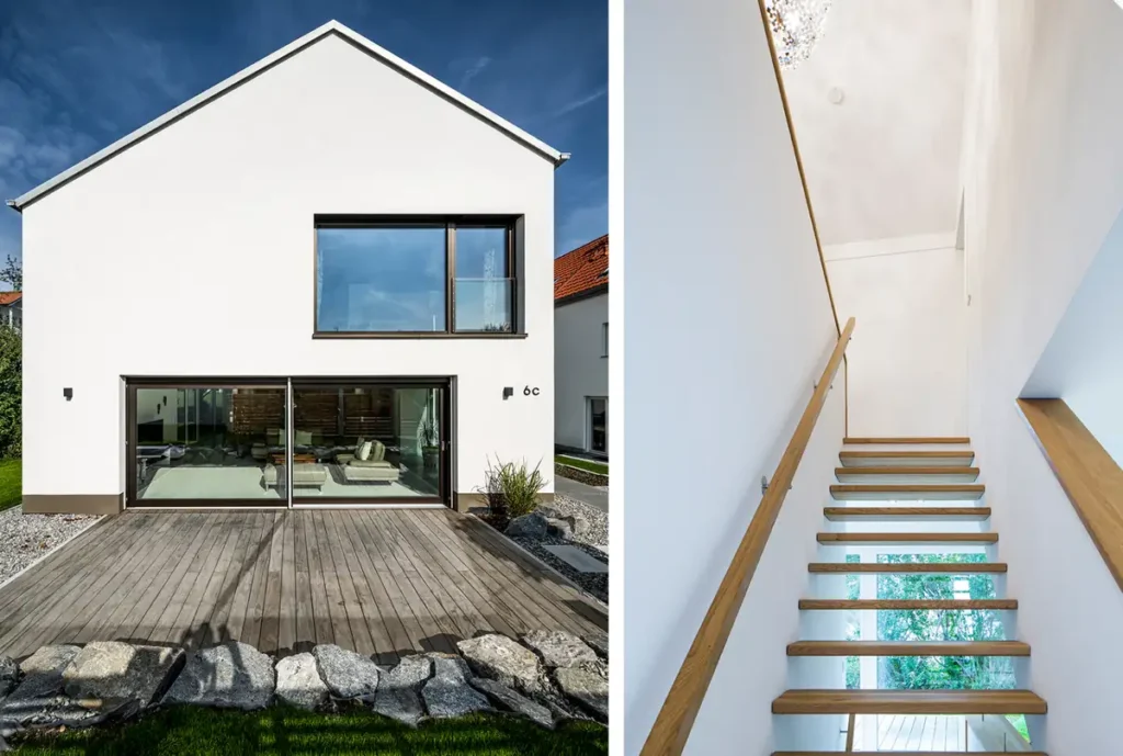 Modernes weißes Haus von außen mit großen Fenstern und Glastüren und einer Holztreppe mit Glasgeländer im Inneren.