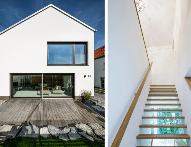 Modernes weißes Haus von außen mit großen Fenstern und Glastüren und einer Holztreppe mit Glasgeländer im Inneren.