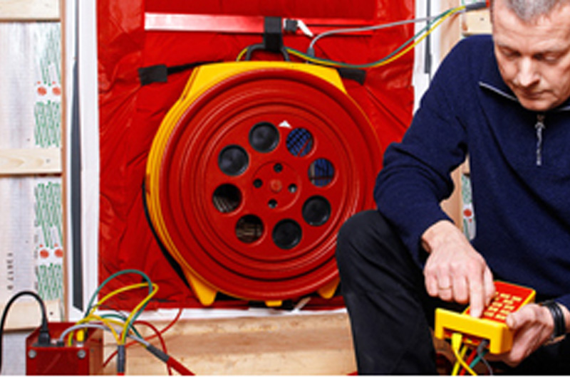 Person, die einen Blower-Door-Testlüfter während einer energieeffizient bauen-Inspektion in einem Gebäude bedient.