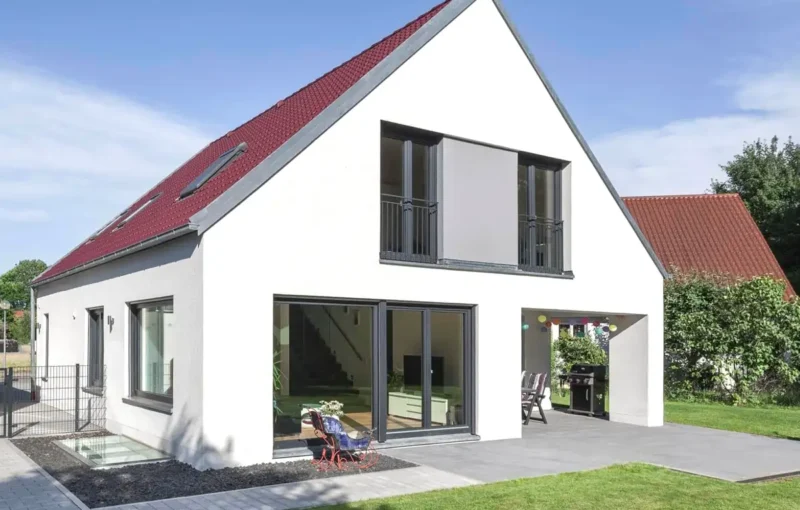 Modernes weißes Haus mit rotem Schrägdach, großen Fenstern und einem kleinen Innenhof vor dem Haus.