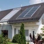 Modernes Haus mit Sonnenkollektoren auf dem Dach, umgeben von einem grünen Rasen und verschiedenen Sträuchern.