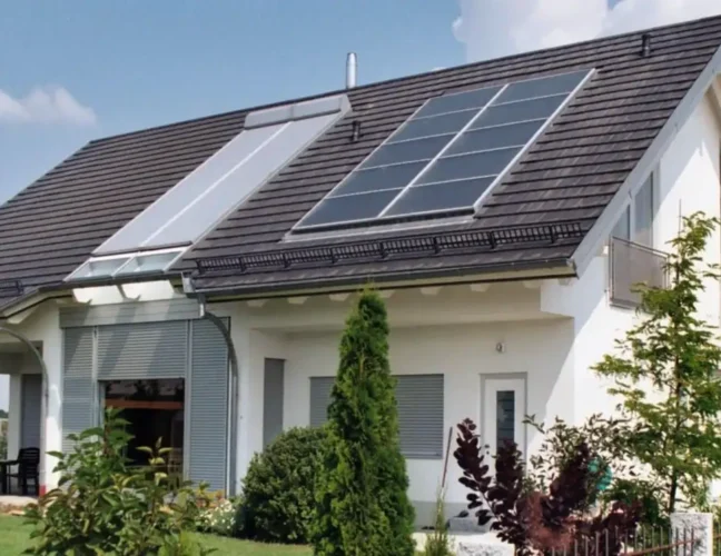 Modernes Haus mit Sonnenkollektoren auf dem Dach, umgeben von einem grünen Rasen und verschiedenen Sträuchern.