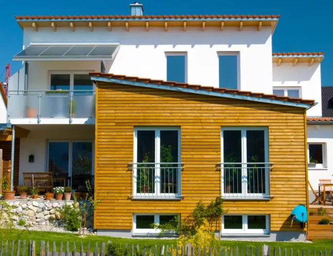 Modernes Haus mit weißen Wänden und einem Holzanbau, großen Fenstern und einem kleinen Vorgarten.