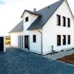 Modernes weißes Haus mit dunklem Dach und freistehender Garage, gepflasterter Einfahrt.