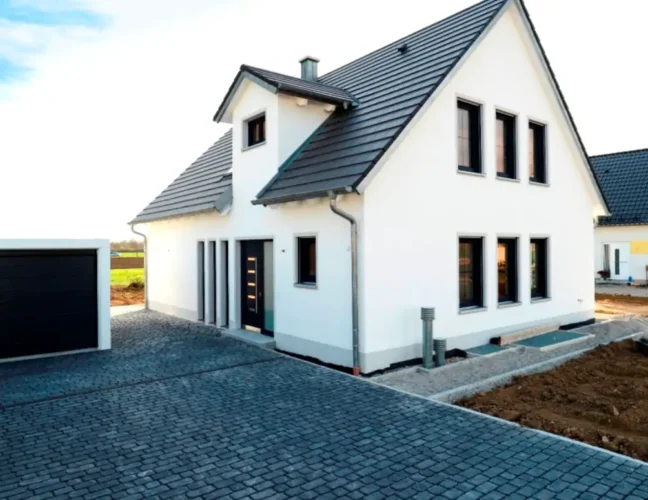 Modernes weißes Haus mit dunklem Dach und freistehender Garage, gepflasterter Einfahrt.