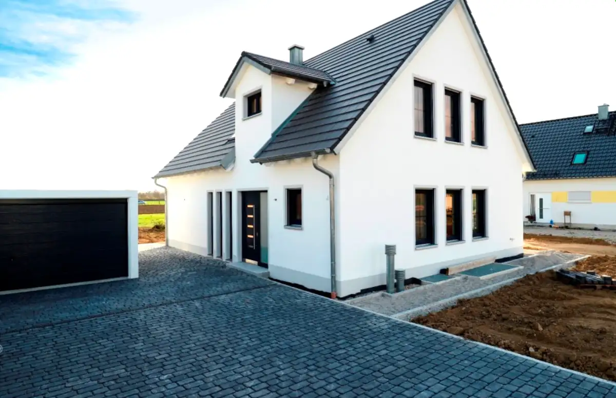 Modernes weißes Haus mit dunklem Dach und freistehender Garage, gepflasterter Einfahrt.