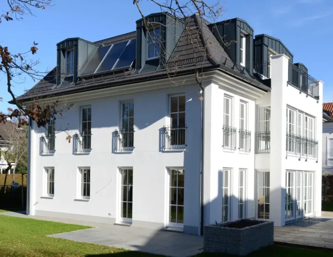 Modernes weißes dreistöckiges Haus mit großen Fenstern und Sonnenkollektoren auf dem Dach an einem sonnigen Tag.