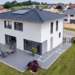 Modernes zweistöckiges weißes Haus mit Terrasse, Sonnenkollektoren und gepflegtem Rasen in einem Vorort.