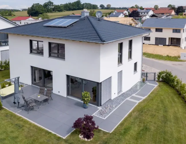 Modernes zweistöckiges weißes Haus mit Terrasse, Sonnenkollektoren und gepflegtem Rasen in einem Vorort.
