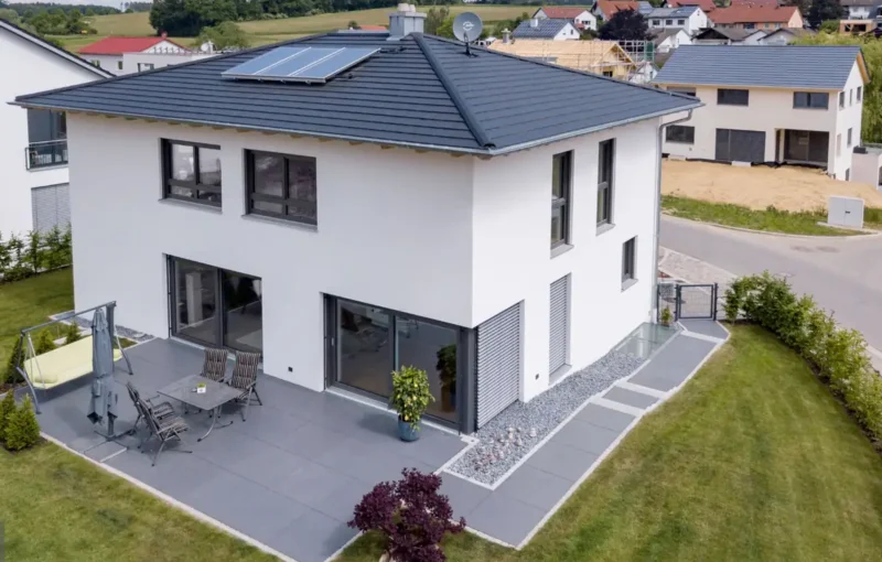 Modernes zweistöckiges weißes Haus mit Terrasse, Sonnenkollektoren und gepflegtem Rasen in einem Vorort.