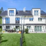 Modernes zweistöckiges weißes Zweifamilienhaus mit großem grünen Rasen und Terrassenmöbeln im Freien.