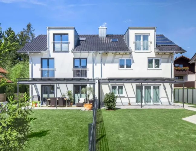 Modernes zweistöckiges weißes Zweifamilienhaus mit großem grünen Rasen und Terrassenmöbeln im Freien.