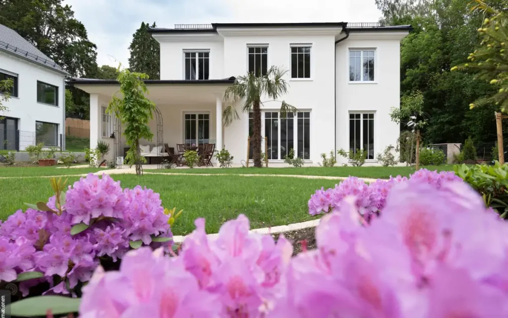 Luxuriöses Einfamilienhaus mit moderner Architektur, Garten und pinken Blumen vor blauem Himmel am Ammersee.