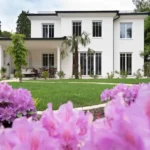 Luxuriöses Einfamilienhaus mit moderner Architektur, Garten und pinken Blumen vor blauem Himmel am Ammersee.