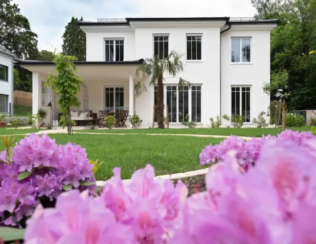 Luxuriöses Einfamilienhaus mit moderner Architektur, Garten und pinken Blumen vor blauem Himmel am Ammersee.
