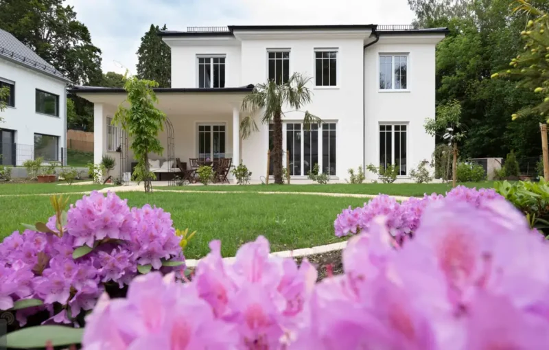 Luxuriöses Einfamilienhaus mit moderner Architektur, Garten und pinken Blumen vor blauem Himmel am Ammersee.