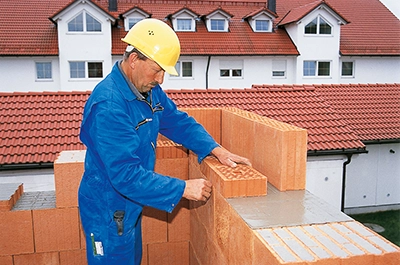 Bauarbeiter mit gelbem Schutzhelm baut energieeffizient bauen Massivhäuser mit Häusern im Hintergrund.