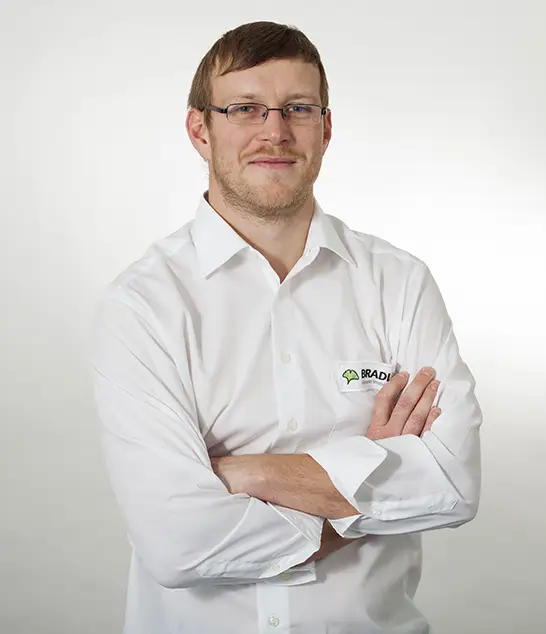 Benjamin Walter mit Brille und weißem Hemd, die Arme verschränkt, steht selbstbewusst als Bauleiter vor einem schlichten Hintergrund.