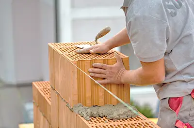 Eine Person beim Verlegen von Ziegeln und Auftragen von Mörtel auf einem Rohbau vom Bauunternehmen BradlBau in Bayern.
